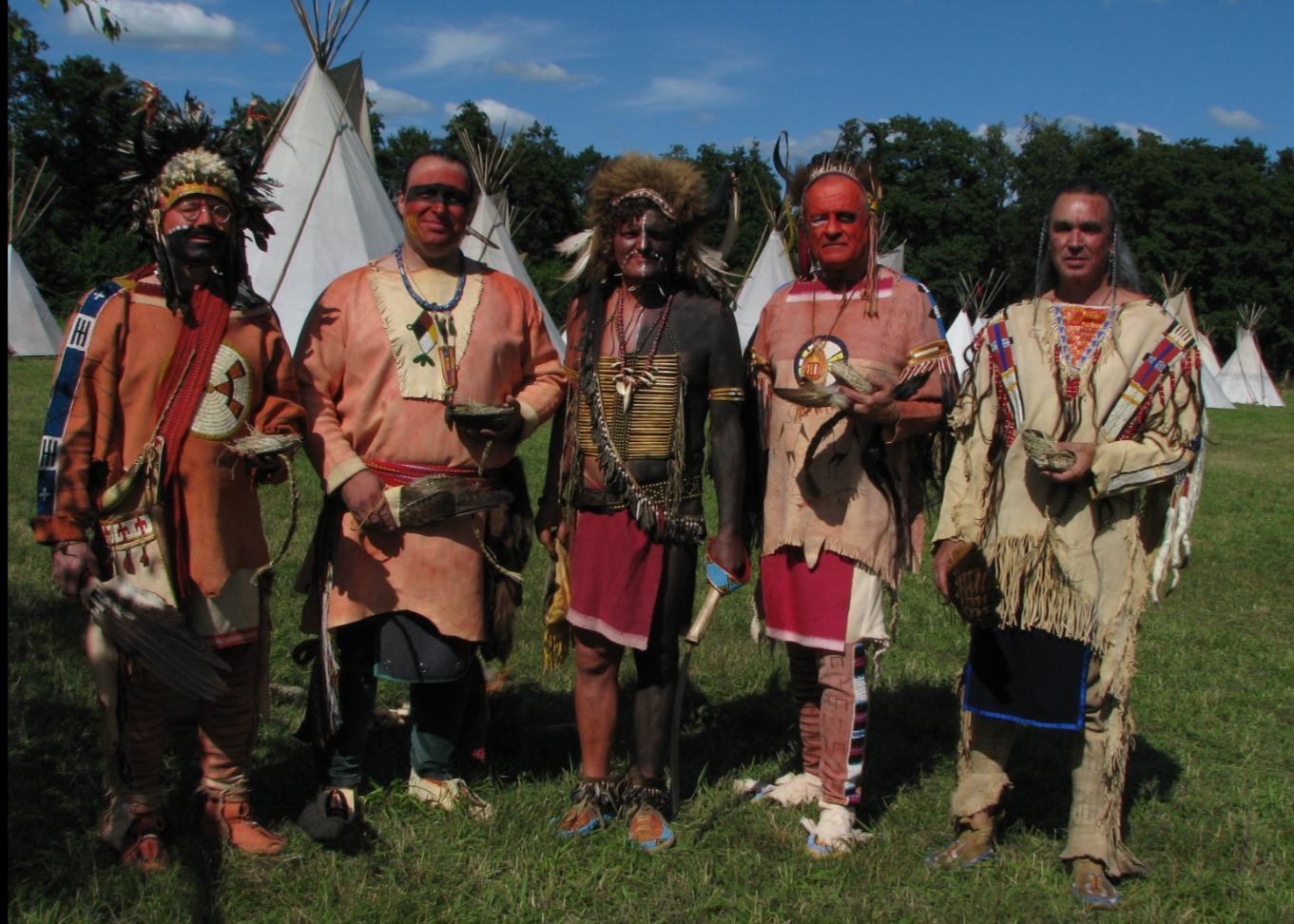Fünf Mitglieder in Kleidung der Plains-Stämme stehen vor Tipis